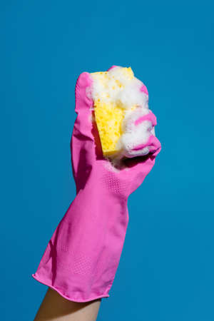 Closeup photo of hand wearing glove and sponge isolated over blue wallの写真素材