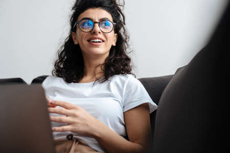 Smiling brunette young woman working with laptop while sitting on sofa at home
