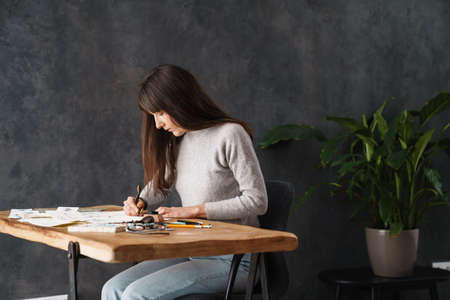 Serious beautiful calligrapher girl writing while working at table indoors