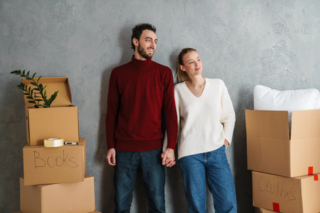 Portrait of a smiling couple moving together in a new house surrounded with boxes, holding handsの写真素材
