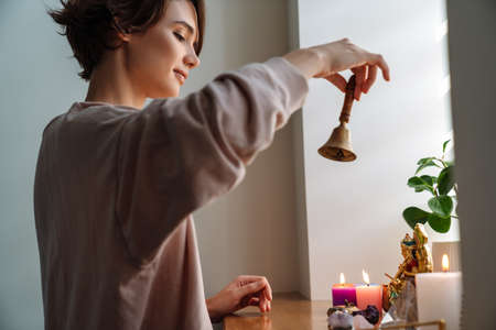 Peaceful girl ringing bell while praying at home shrine indoorsの写真素材