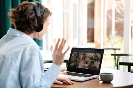 Back view of a happy attractive young woman in headphones on a video call via laptop computer while...
