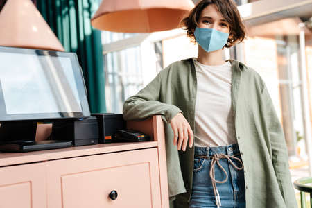 Cheerful beautiful girl in protective mask posing at cafe indoors