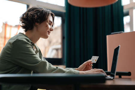 Pleased girl using credit card while working with laptop in cafe indoorsの写真素材