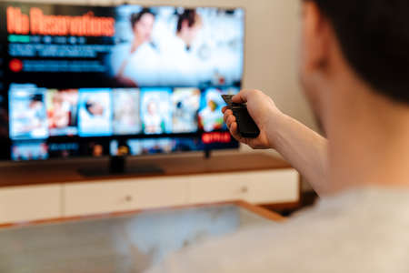 Man watching tv and eating popcorn at home on a couch, back view