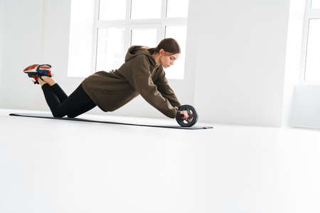 Athletic young sportswoman doing push-ups with equipment while working out on mat indoors