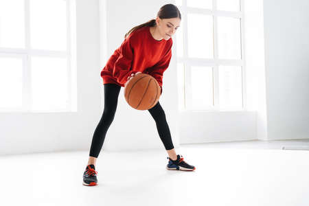 Athletic young sportswoman working out with basketball indoorsの写真素材