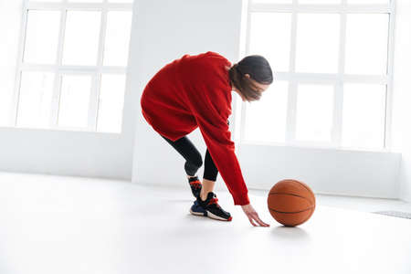 Athletic young sportswoman working out with basketball indoorsの写真素材