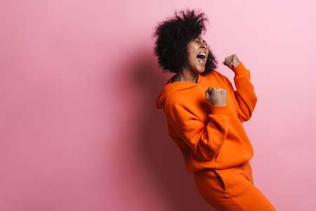 Delighted african american girl screaming and making winner gesture isolated over pink background