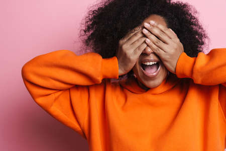 Excited african american woman covering her eyes and screaming isolated over pink backgroundの写真素材