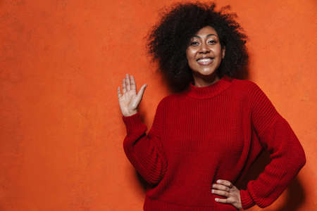 Happy african american girl smiling and showing her palm isolated over orange wall