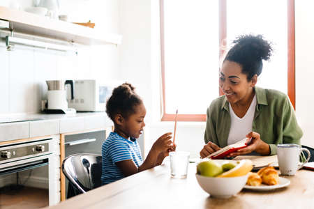 Happy mother drawing with her daughter at table in home kitchenの写真素材