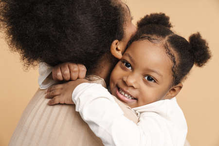 Happy black mother and daughter hugging and smiling isolated over beige backgroundの写真素材