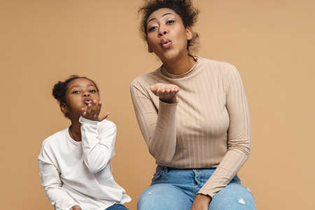 Happy black mother and daughter blowing air kiss at camera isolated over beige backgroundの写真素材