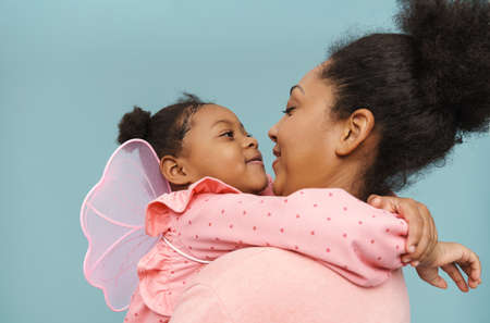 African mother and daughter smiling and hugging together isolated over blue wallの写真素材