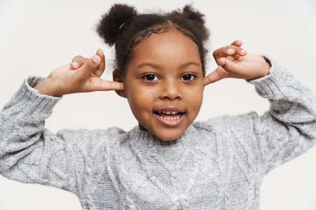 African curly girl wearing sweater plugging her ears isolated over white wall