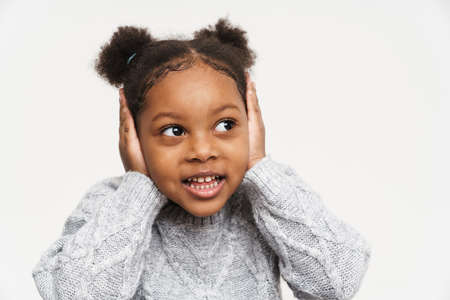 African curly girl wearing sweater covering her ears isolated over white wallの写真素材