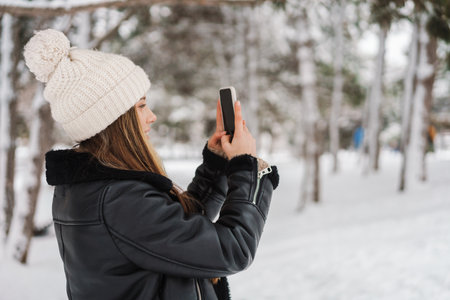 Happy girl taking photo on cellphone while walking in winter forestの写真素材