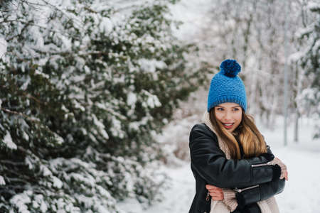 Happy beautiful girl in knit hat smiling while walking in winter parkの写真素材