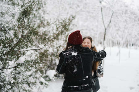 Happy beautiful girls playing snowballs while walking in winter forestの写真素材