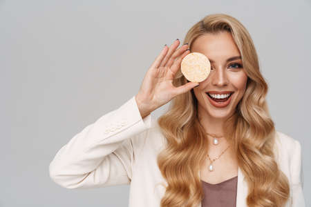 Happy gorgeous woman smiling while posing with cosmetic sponge isolated over grey backgroundの写真素材