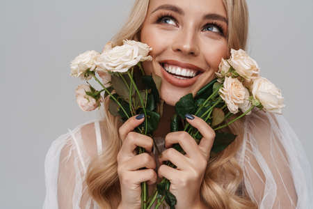 Beautiful happy girl smiling while posing with roses isolated over grey backgroundの写真素材