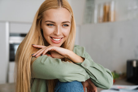 Happy blonde young woman smiling and looking aside at home kitchenの写真素材