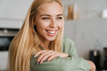 Happy blonde young woman smiling and looking aside at home kitchenの写真素材