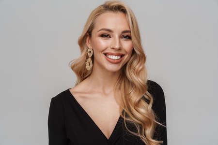 Happy girl in luxury earrings smiling and looking at camera isolated over grey backgroundの写真素材