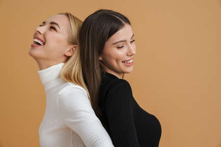 Beautiful laughing women posing back to back on camera isolated beige background
