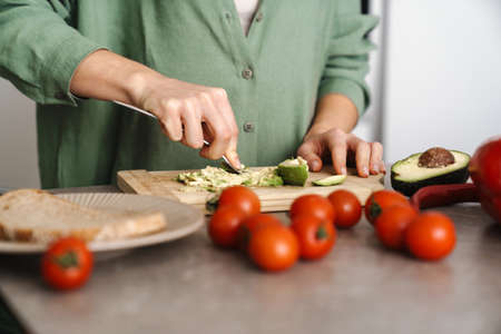 Caucasian woman preparing sandwich with avocado at home kitchenの写真素材