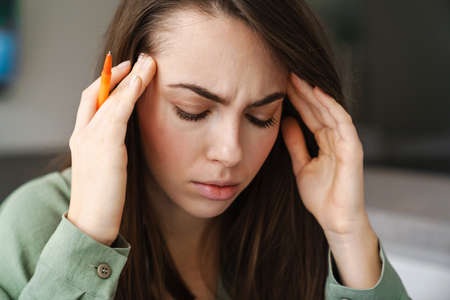 Young unhappy woman with headache rubbing her temples indoors
