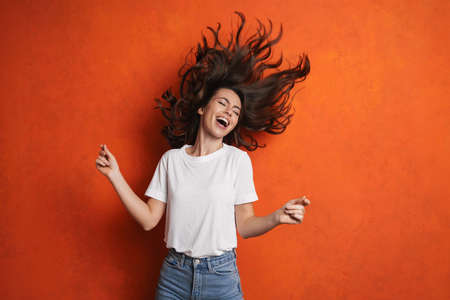 Excited beautiful girl singing and dancing on camera isolated over orange wall