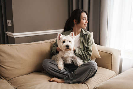 Happy white woman resting with her dog on sofa at homeの写真素材