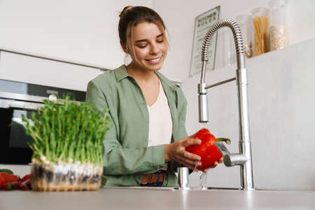 Happy beautiful woman smiling while washing bell pepper at home kitchenの写真素材