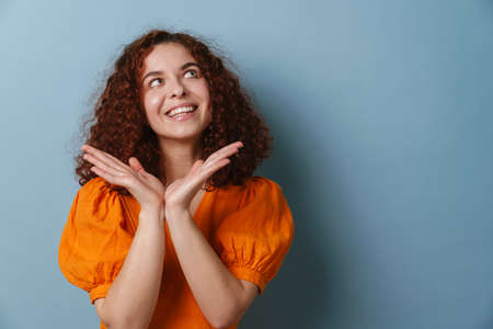 Happy redhead curly girl smiling and holding copyspace isolated over blue background