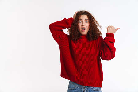 Shocked ginger girl holding on her head and pointing finger aside isolated over white backgroundの写真素材
