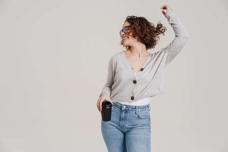 miling attractive young woman in casual wear holding takeaway coffee cup isolated over white...