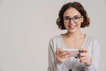 Portrait of an attractive happy young girl in casual clothes using mobile phone isolated over white...