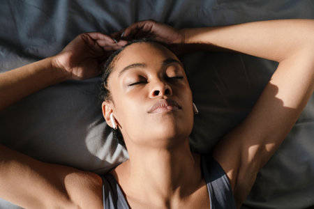 Relaxed african american girl listening music with earphones while lying on bed at home