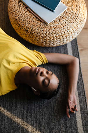 Smiling african-american girl listening to music in earphones, lying on floor, relaxing at home, top viewの写真素材