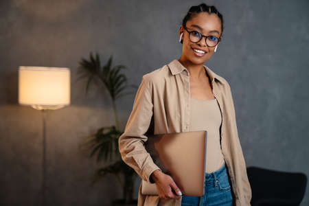 Cheerful young african businesswoman holding laptop computer while standing in the office