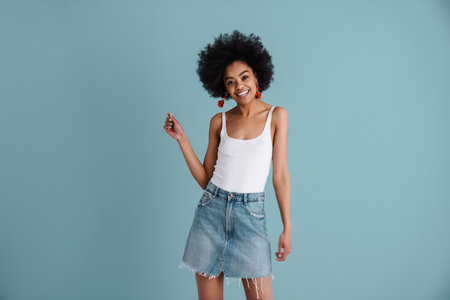 Happy african american girl smiling and looking at camera isolated over blue backgroundの写真素材