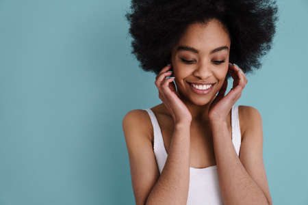 Happy african american girl posing and smiling at camera isolated over blue backgroundの写真素材