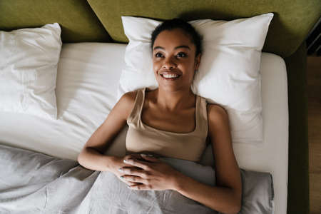 Happy african american girl smiling while lying in bed after sleep at home