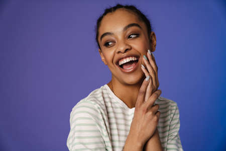 Young black woman in t-shirt laughing and looking aside isolated over blue background
