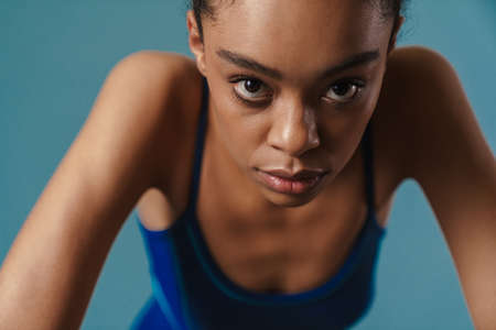 Close up portrait of a young african woman in swimsuit standing over blue wallの写真素材