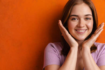 Young ginger happy woman gesturing and smiling at camera isolated over orange wallの写真素材