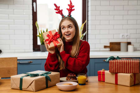 Happy young girl wearing pajamas celebrating christmas at the kitchen table, opening presentsの写真素材