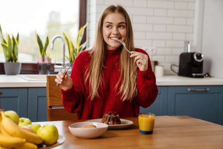 Cheerful young girl eating christmas cake while sitting at the kitchen